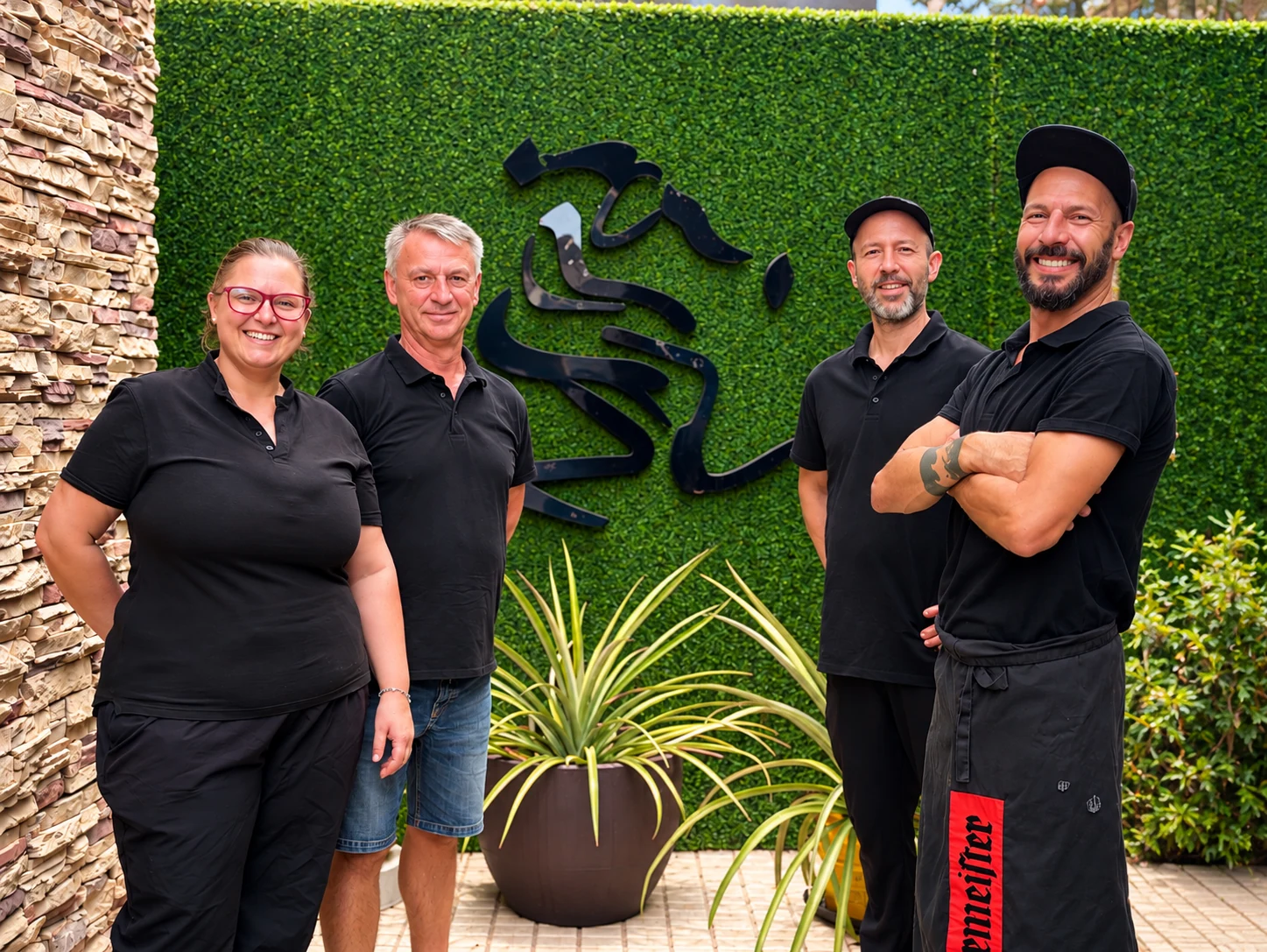Cuatro miembros del equipo de Eulenspiegel Tenerife delante de la pared verde con el logotipo del restaurante